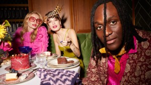 Three fashionable people in evening clothes sitting around a table and eating a gourmet dinner