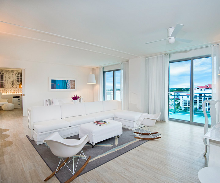 Spacious living room with a large white couch, chair and floor-to-ceiling windows opening to a balcony with Caribbean views. 