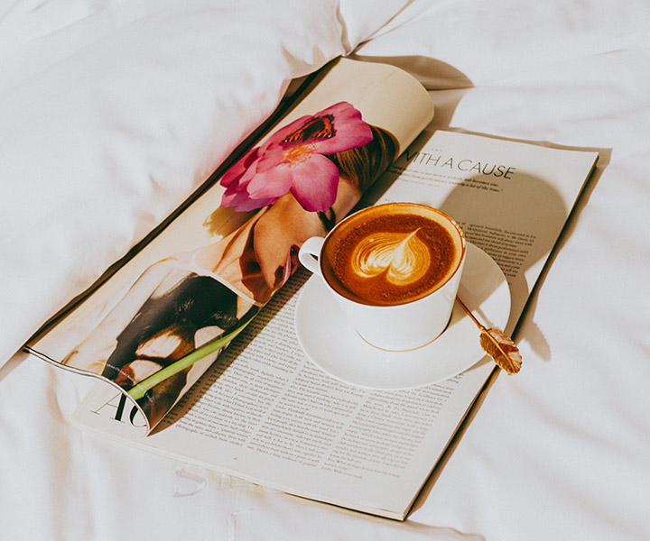 café e uma revista aberta sobre uma capa de edredão branca