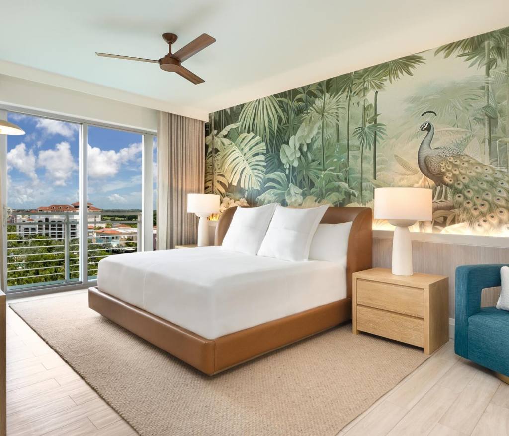 a king bed in a leather bed frame with two bedside tables and tropical wallpaper on the walls