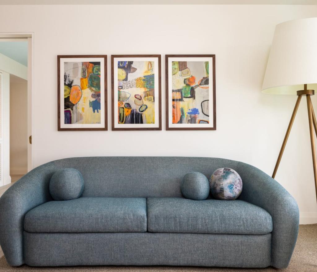 a blue couch up against a wall with three distinct pieces of art next to a large floor lamp