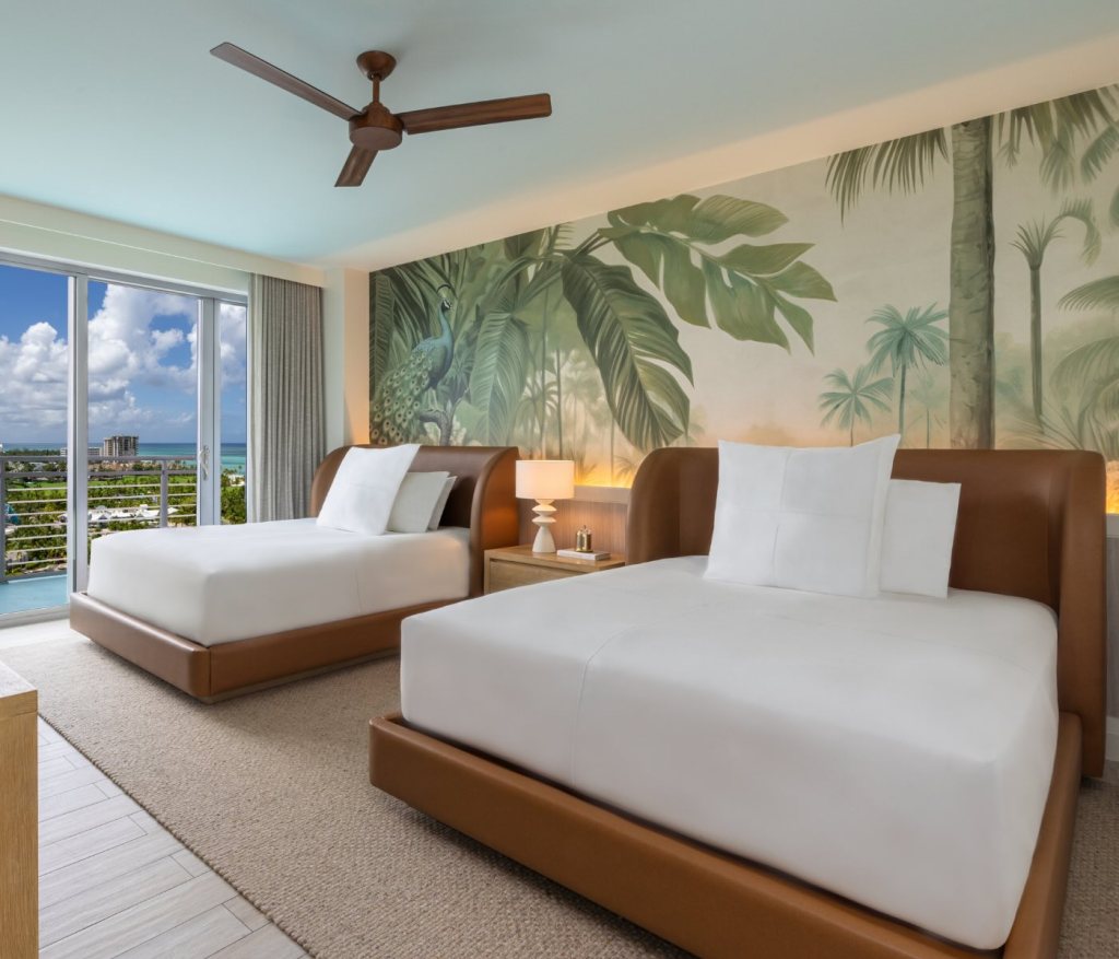 a bedroom with two beds and tropical wallpaper and ceiling fan