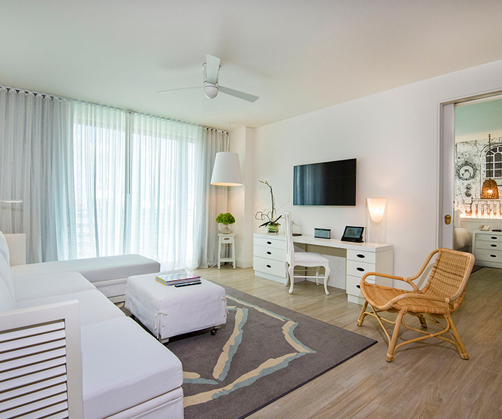 sala de estar de suite com televisão montada na parede, cadeira de palhinha e sofá branco