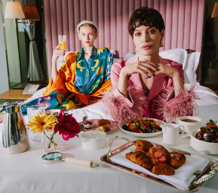 Two elegant ladies enjoying a delightful morning on a luxurious bed, savoring a scrumptious breakfast spread.
