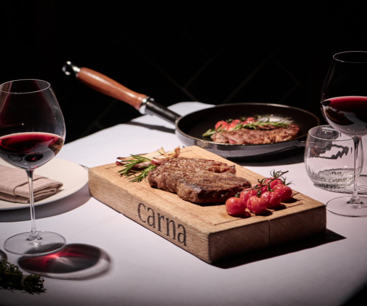 a mouthwatering steak plated with fresh tomatoes and two glasses of delicious red wine
