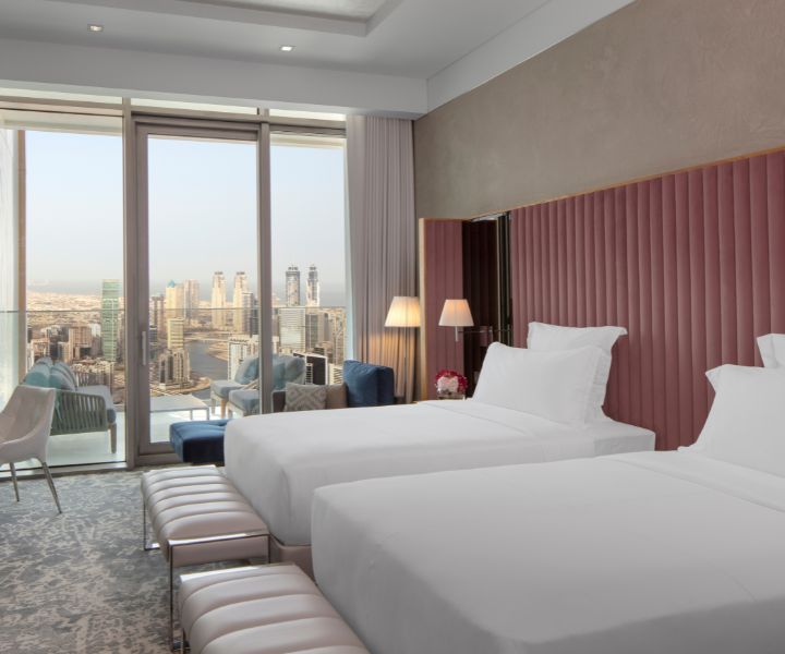 Luxurious bedroom with two beds, elegantly accompanied by a stylish lamp and pink headboard with city views. 