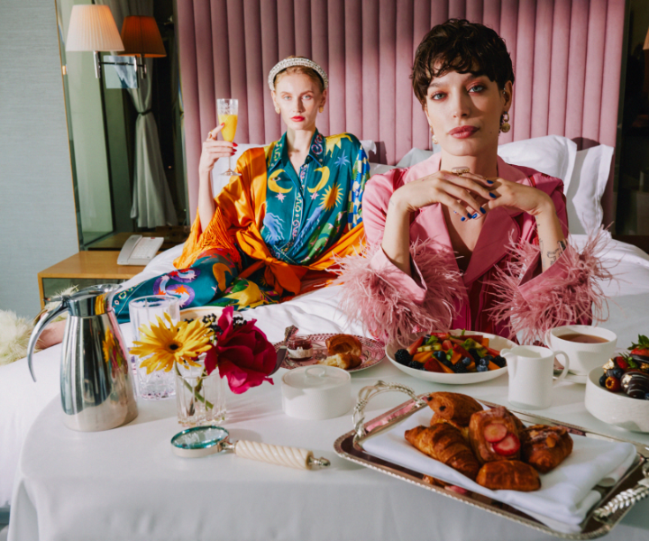 Two elegant ladies enjoying a delightful morning on a luxurious bed, savoring a scrumptious breakfast spread.
