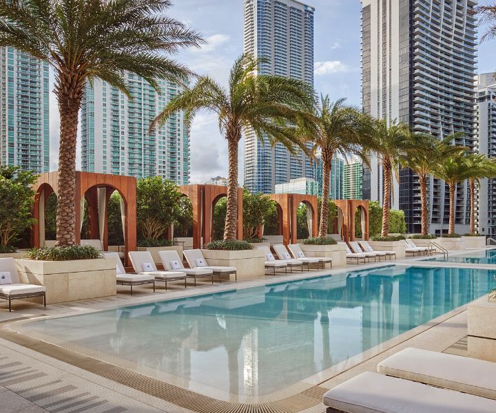 Luxurious rooftop pool at SLS LUX Brickell, surrounded by palm trees, cabanas and lounge chairs.