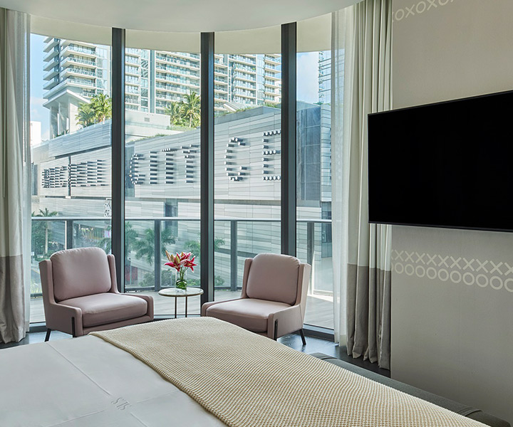 a king bedroom with a mounted HDTV, and seating area adjacent to the floor to ceiling windows.