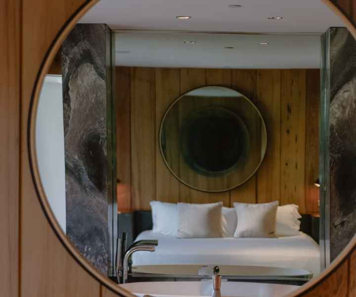 Espejo con reflejo de una habitación de invitados con cama y espejo en la pared. 