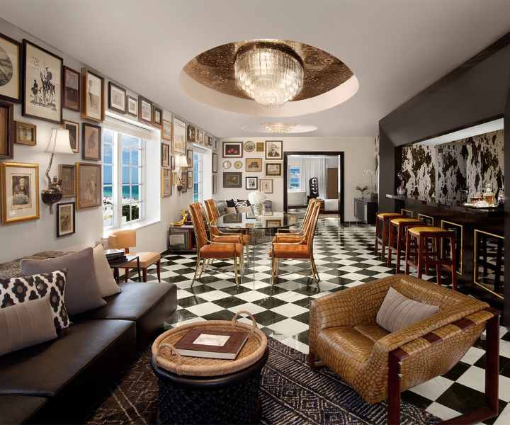 Habitación estilo salón con suelos a cuadros blancos y negros, sofás de cuero y una lámpara de araña. 