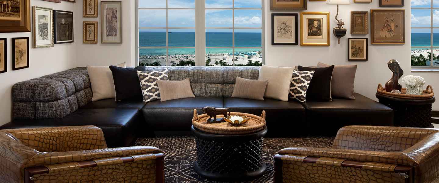 Living room style room in the SLS South Beach Tower Penthouse with leather couches and chairs, with a view of the ocean in the background. 