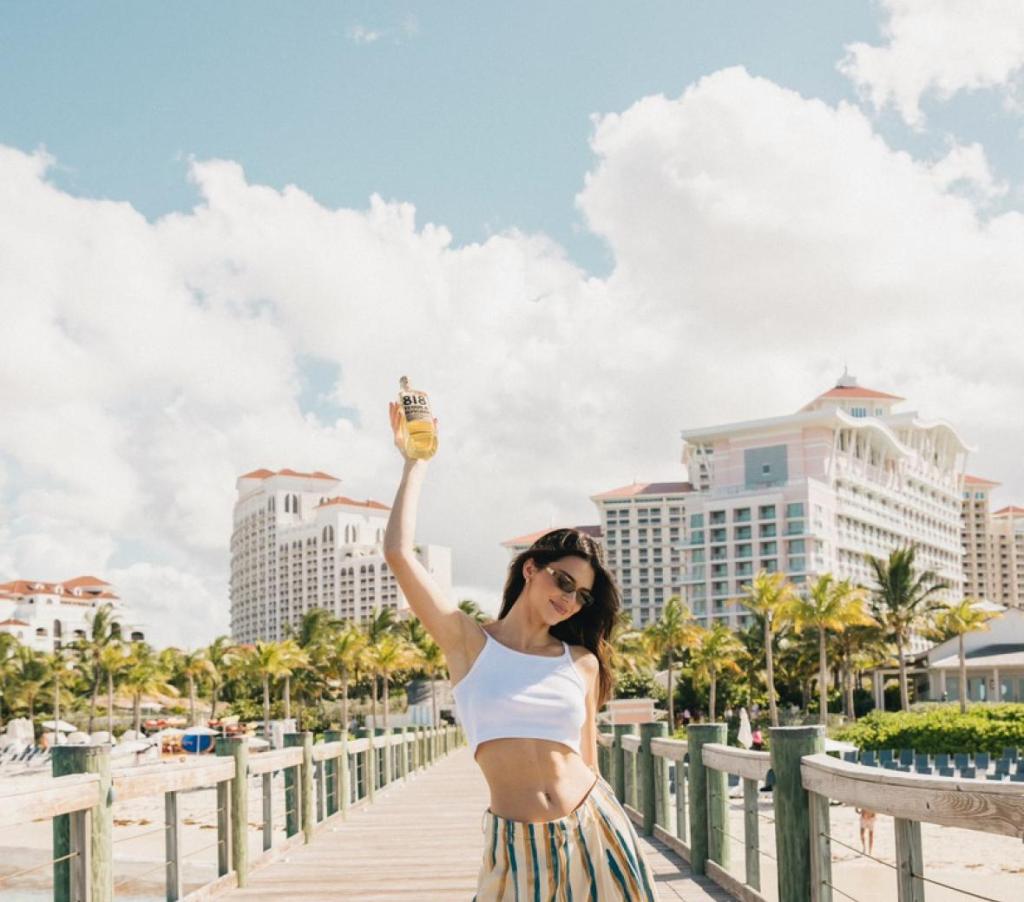 Woman (Kendall Jenner) in white top and striped skirt standing on dock, promoting 818 Tequila.
