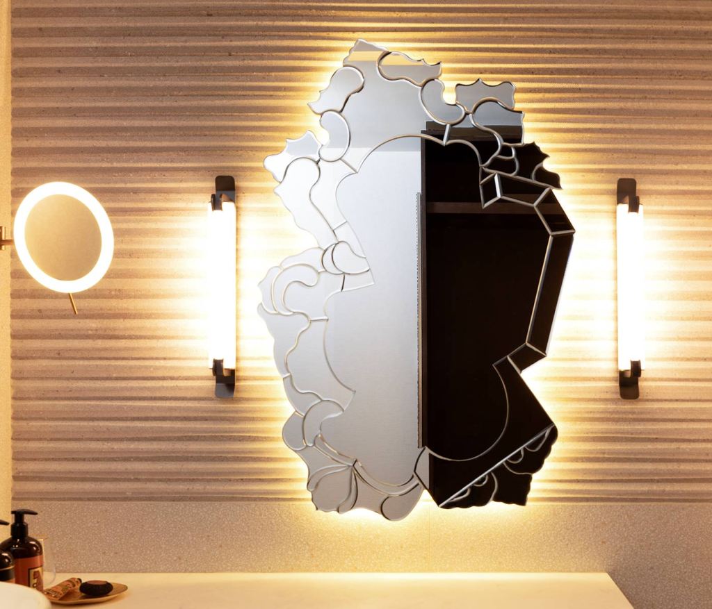 A decoratively shaped mirror flanked by two cylindrical bathroom sconces