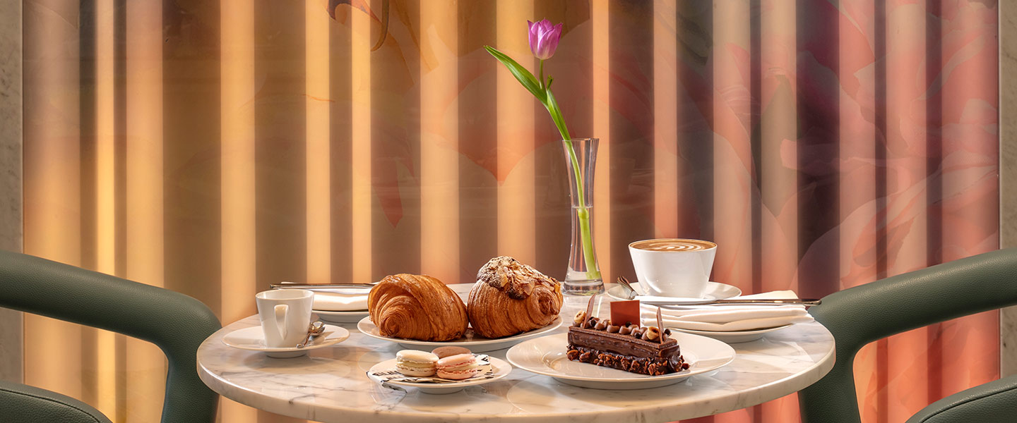 Mesa de café com pastelaria, café e uma tulipa num vaso