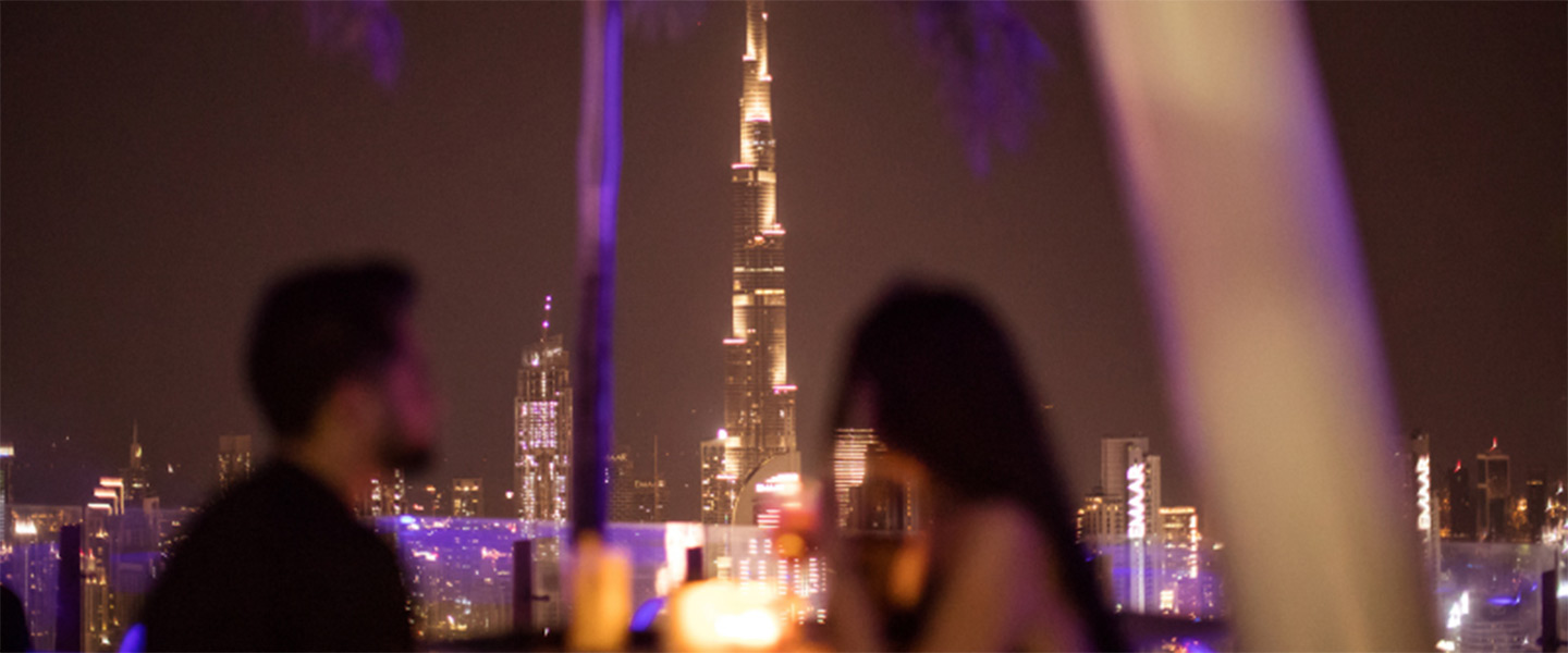 Dos personas en una azotea con vistas a la ciudad de Dubái por la noche