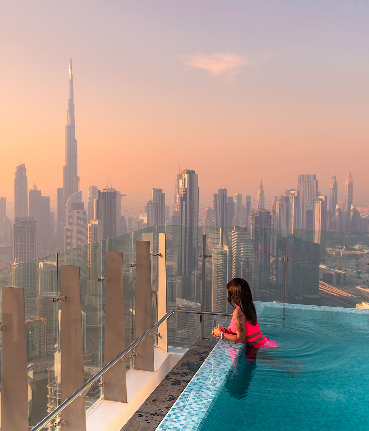 Woman swimming in the 75th floor rooftop infinity pool, overlooking the Burj Khalifa and Dubai at sunset
