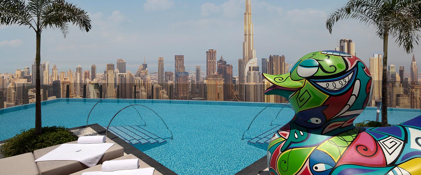 La piscine sur le toit du 75e étage du SLS Dubaï, avec une statue de canard surdimensionnée et colorée et la ville de Dubaï en arrière-plan