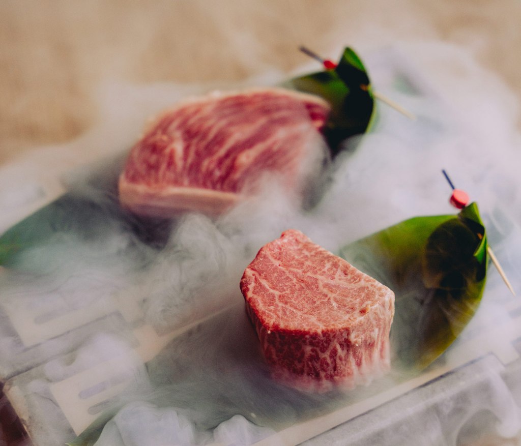 Two raw steaks presented in dry ice, sitting on tropical leaves