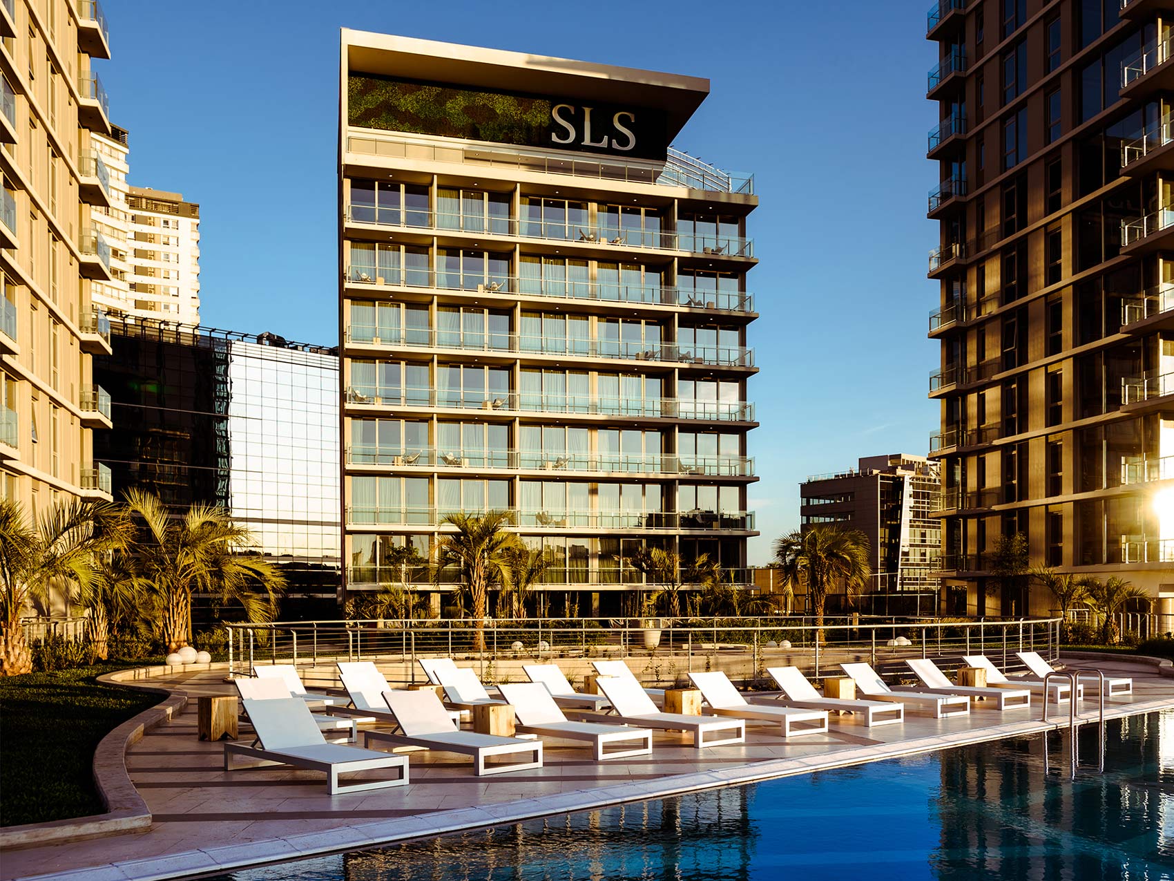 Modern metal and glass exterior of SLS Puerto Madero hotel, overlooking a pool with lounge chairs.
