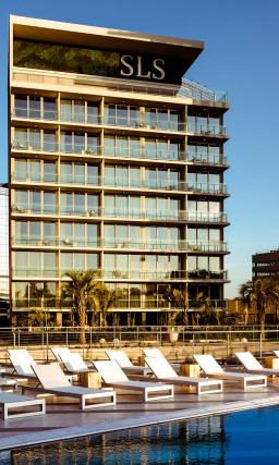 Modern metal and glass exterior of SLS Puerto Madero hotel, overlooking a pool with lounge chairs.