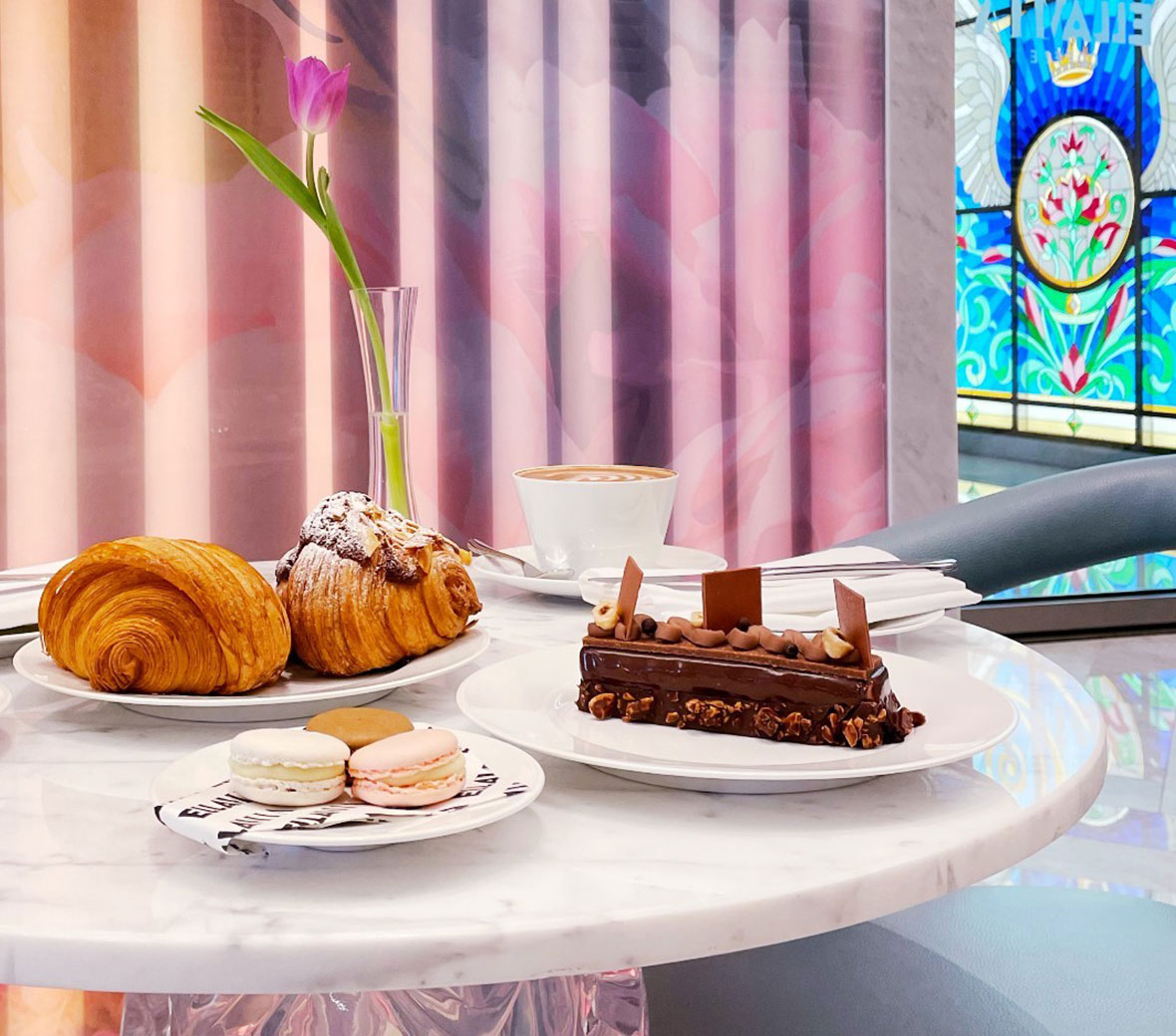 A table at EllaMia at SLS Dubai with pastries and coffee placed in front of a beautiful stained glass window.