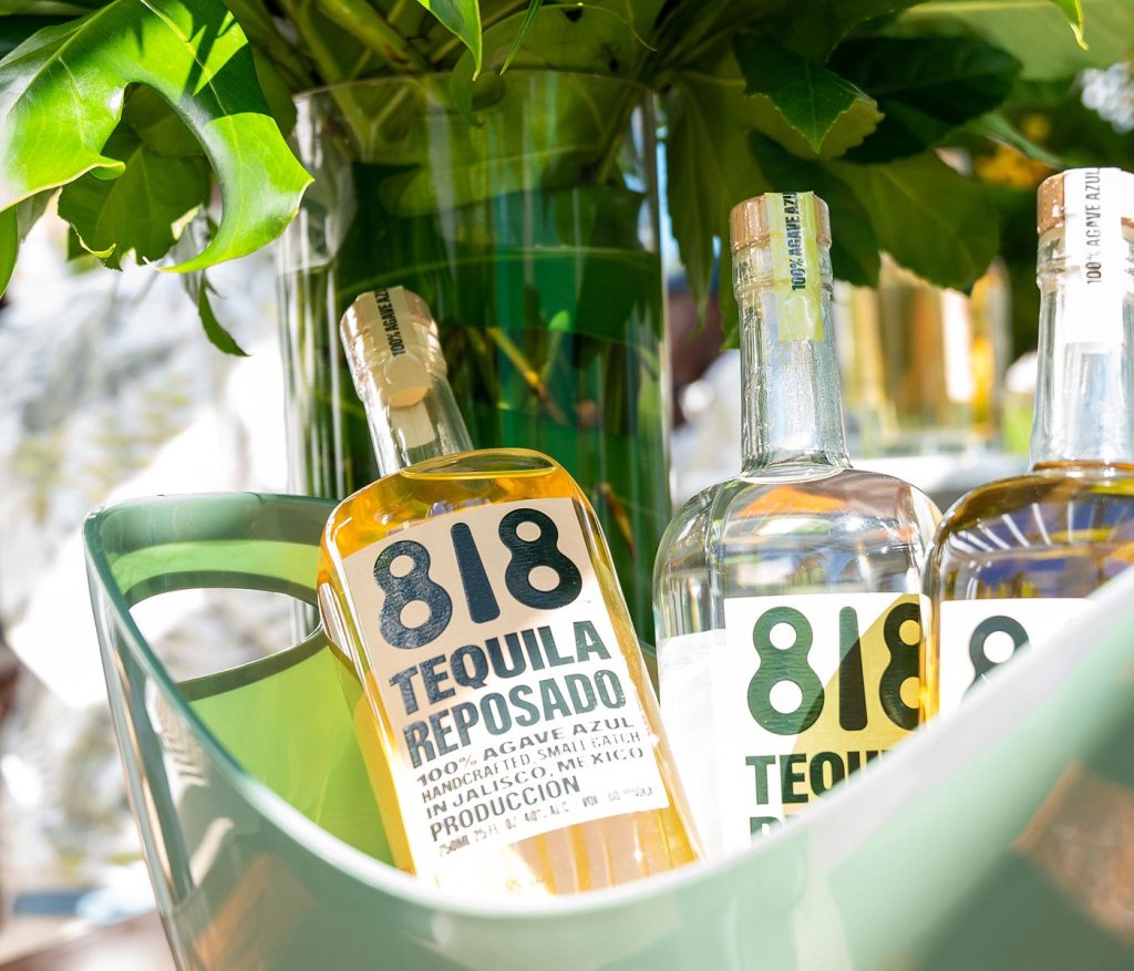 3 bottles of 818 tequila in a green ice bucket with greenery behind them
