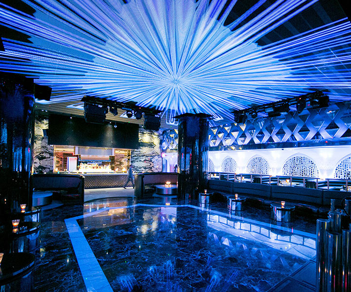 Un bar con una vibrante luz azul que lo ilumina, creando una cautivadora pista de baile en la discoteca Bond en SLS Baha Mar.