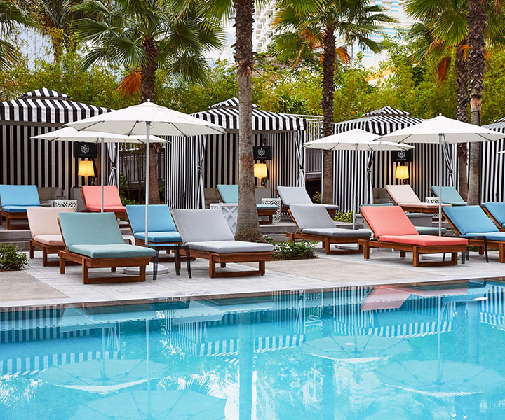 Poolside sun loungers surrounded by palm trees and umbrellas.