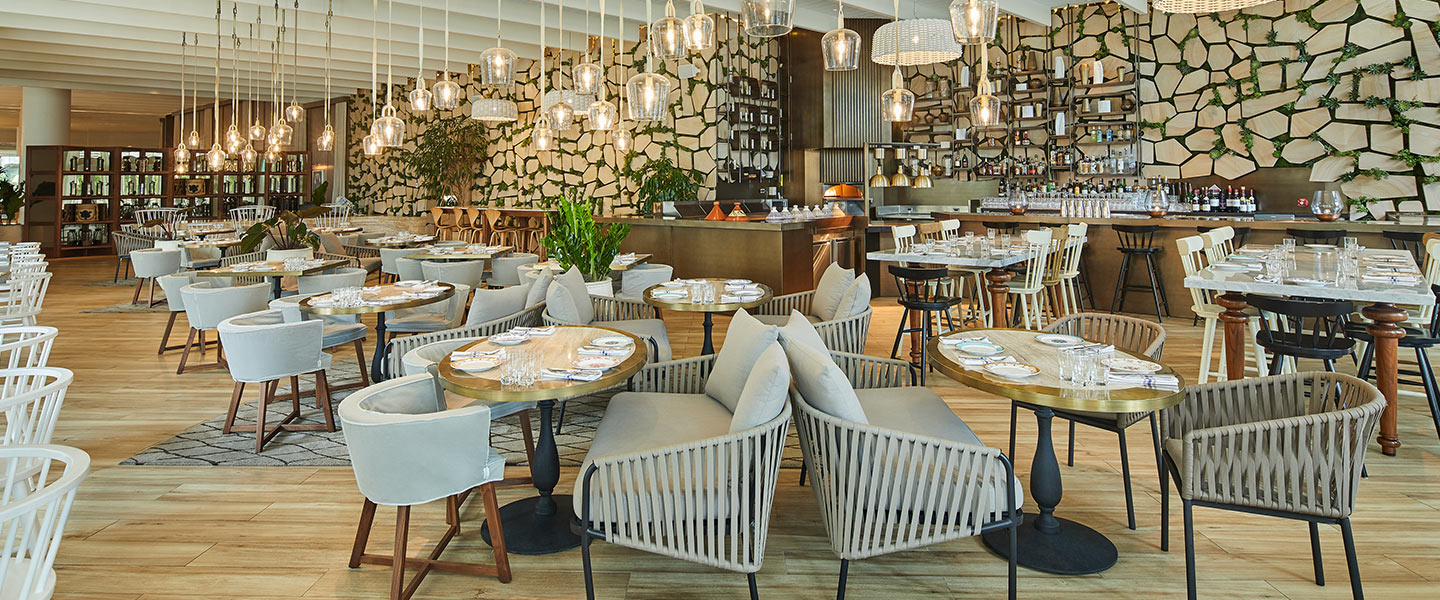 Interior of Cleo Baha Mar restaurant with many tables and chairs for guests and modern hanging lights.