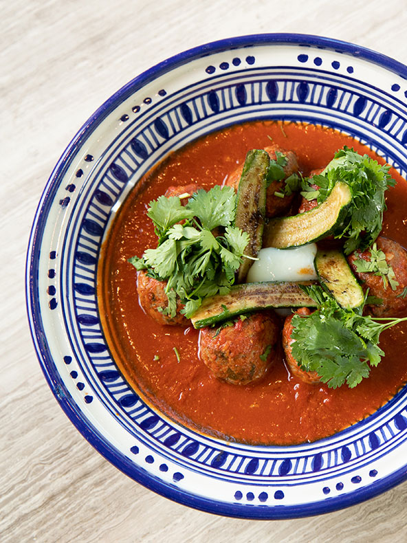 Un plato de comida con un colorido surtido de verduras, albóndigas en salsa roja y guarnición.