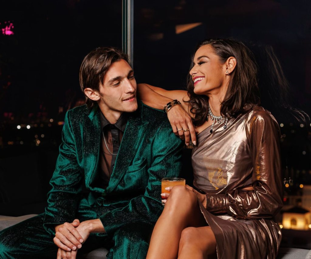 a couple in glam outfits sitting at a bar