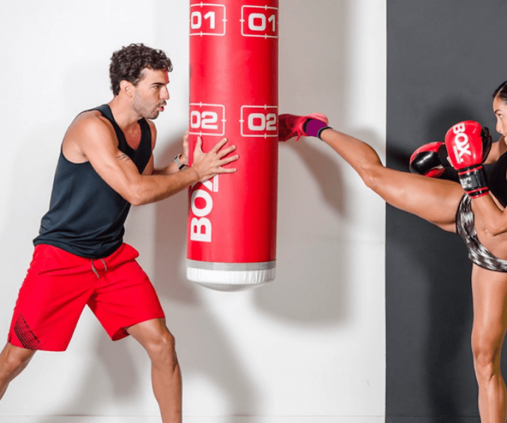 a woman kickboxing into a red kick pad held by a man