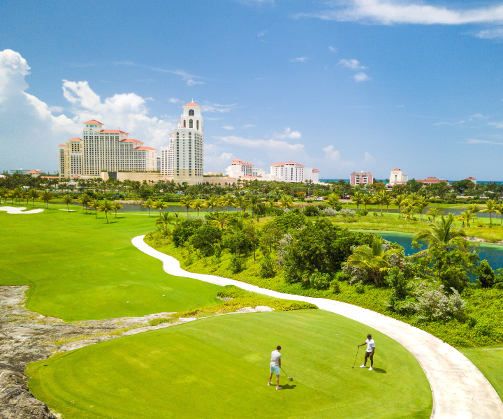 Dos personas en un espectacular campo de golf con el Hotel Baha Mar de fondo