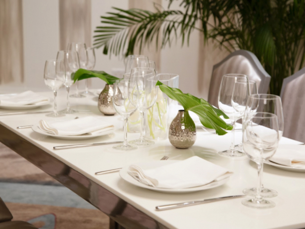 A beautiful table setting with white napkins, places, silverware and silver vases with a leaf.