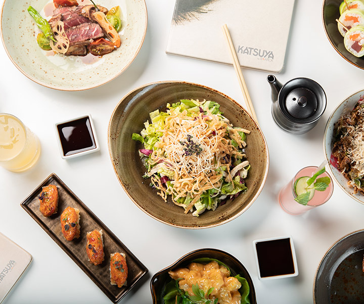 A table filled with a variety of delicious food and refreshing drinks at Katsuya restaurant.