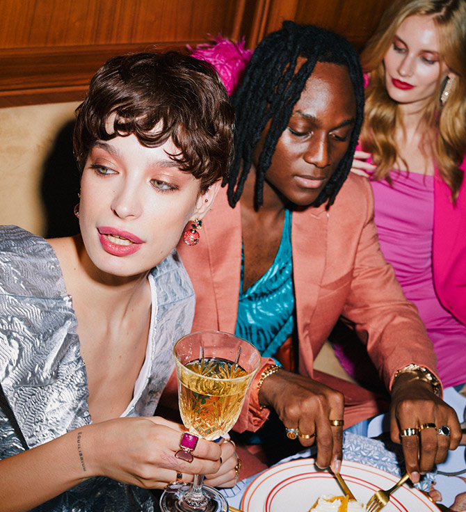 Un hombre y dos mujeres elegantes sentados a una mesa, disfrutando de la deliciosa comida y bebida