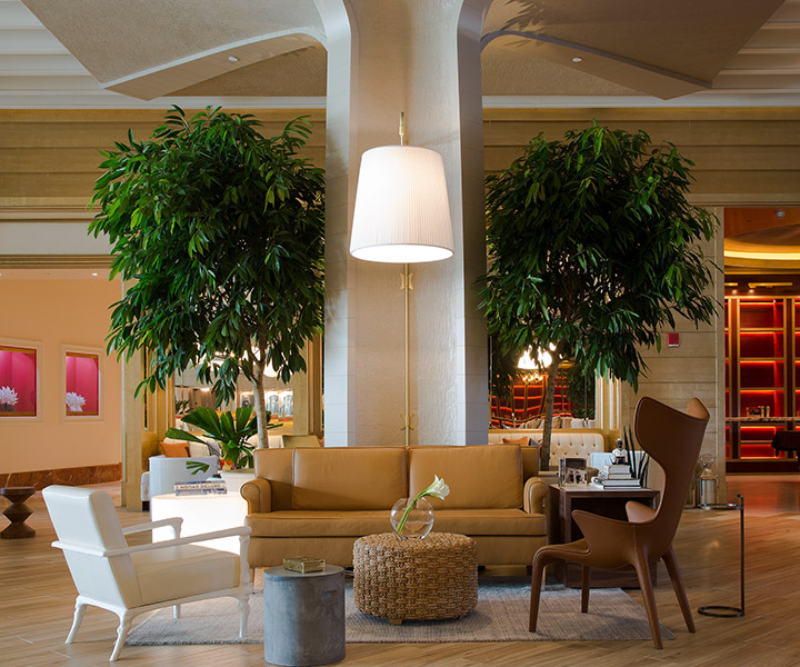 A cozy corner of Monkey Bar, SLS Baha Mar's lobby bar, with an oversized lamp, leather couches and trees.