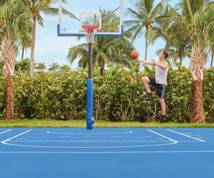 um homem a saltar para lançar uma bola de basquetebol num cesto num campo azul ao ar livre