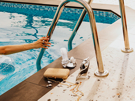 Par de sapatos de salto prateados e mala clutch ao lado da piscina