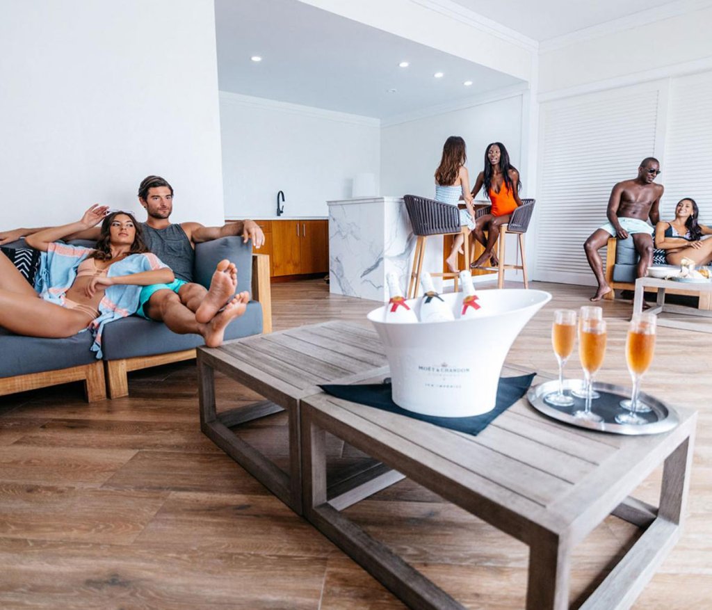 Seis pessoas a relaxar numa grande cabana à beira da piscina com champanhe