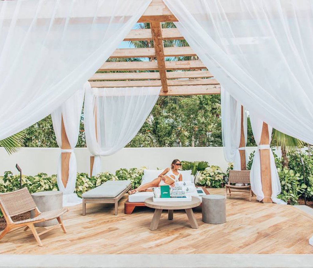 Grande cabana com cortinas transparentes, com uma mulher a descansar