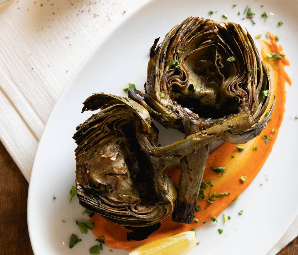 Un plat d’artichauts rôtis capturé au-dessus de la tête et servi avec une sauce rouge-orange vibrante