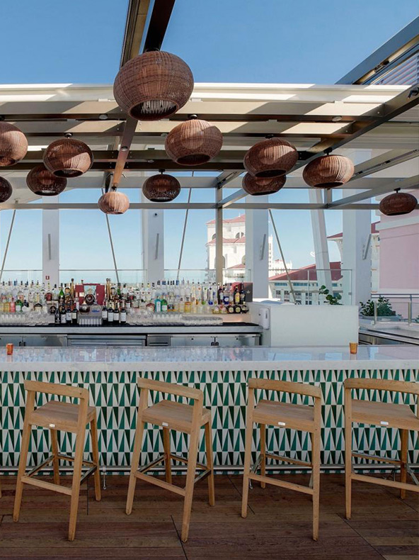 Bar coloré au Skybar, sur le toit du SLS Baha Mar, avec des sièges de bar en bois et des lumières suspendues dans des paniers en osier brun.