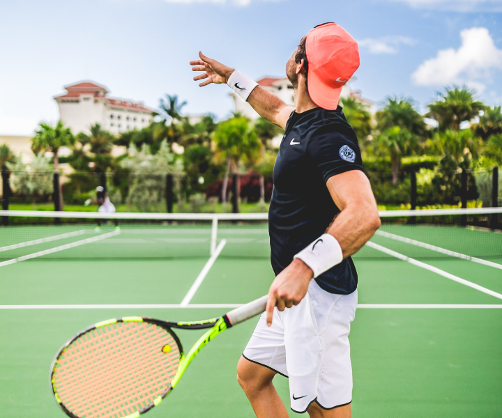 un homme en tenue de sport avec un chapeau rose saumon servant au tennis