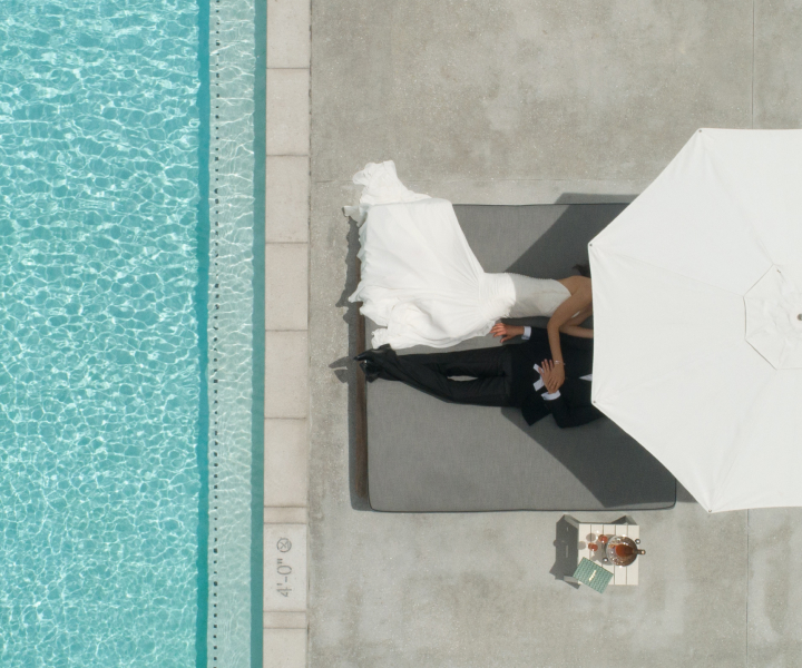 La novia y el novio se relajan bajo la sombrilla junto a la piscina