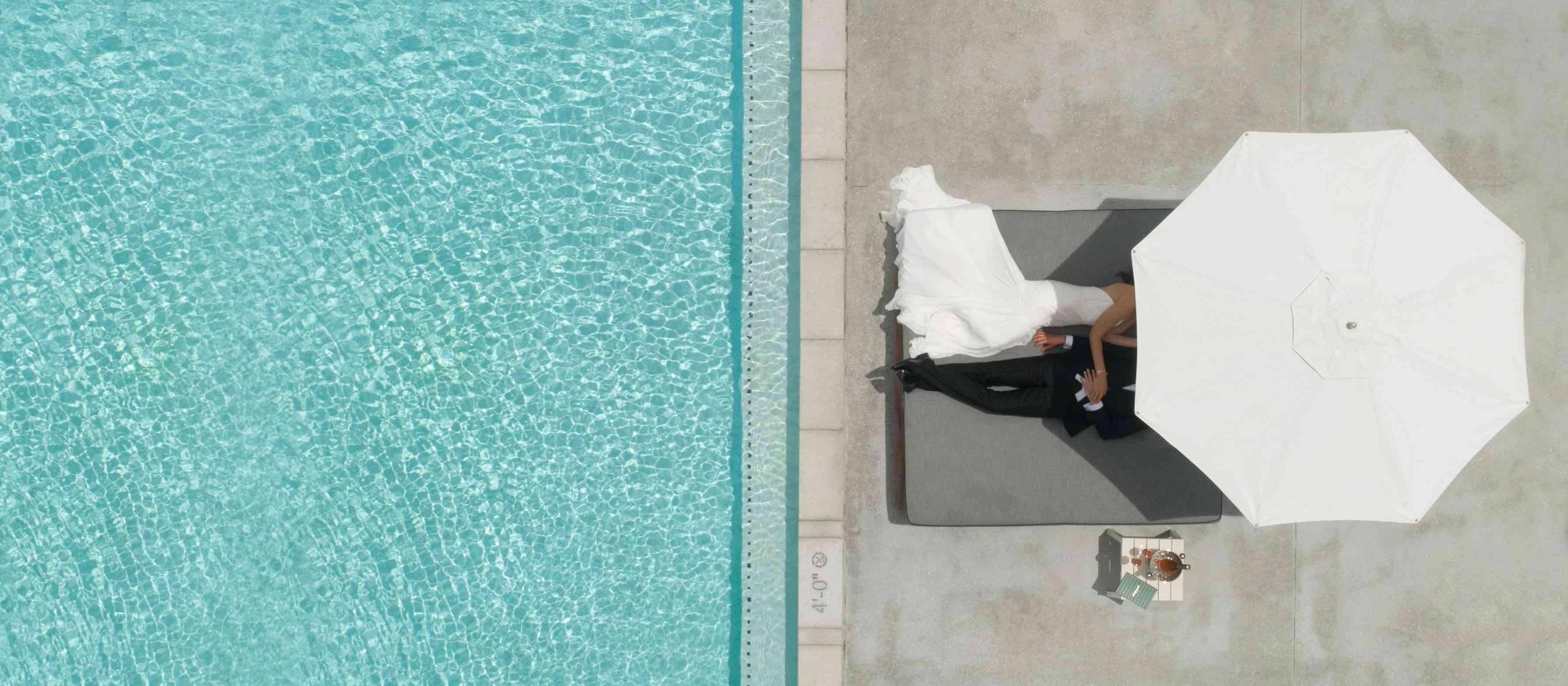 Bride and grooming chilling under the parasol by the pool