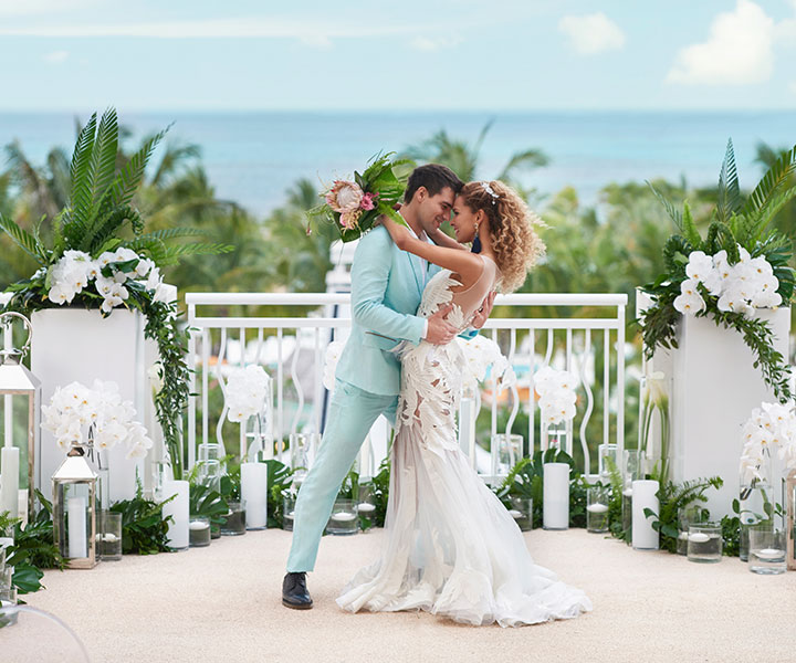 Um casal de noivos abraça-se durante a cerimónia de casamento, contemplando a deslumbrante vista para as palmeiras e o oceano