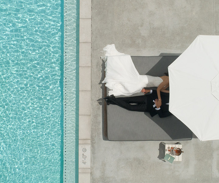A noiva e o noivo a relaxar sob o guarda-sol junto à piscina