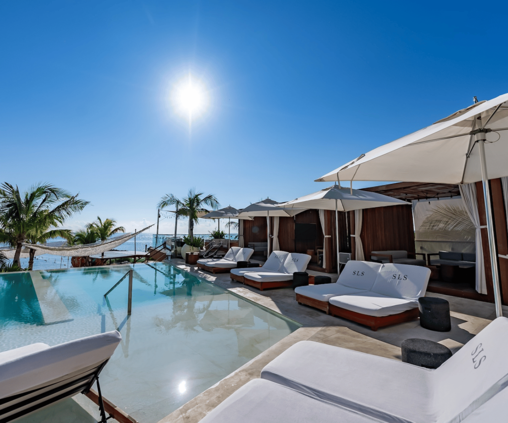 a beautiful pool surrounded by palm trees with luxurious white lounge chairs surrounding it.